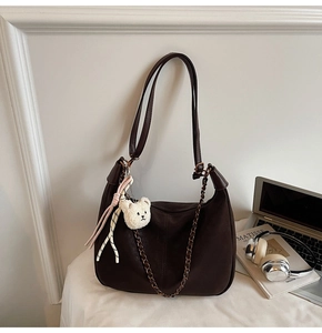 Detail of dark brown dumpling bag with bronze chain and cute plush bear charm on a table