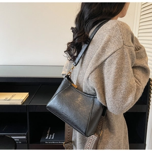 Detail of vintage black PU leather crescent bag featuring dual straps and bronze hardware
