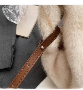 Dettaglio della tracolla in pelle marrone su una borsa a mano in pelliccia sintetica beige