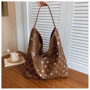 Close-up of brown tote bag featuring silver metal rivets on a soft leather surface