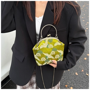 Detailed embroidery of white cranes on a green brocade crossbody bag with metal frame