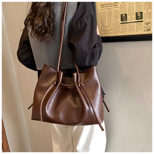 Brown leather tote bag featuring a decorative knot drawstring detail shown on a shoulder