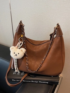 Retro brown hobo shoulder bag with metal chain strap and cute plush bear charm on a sofa