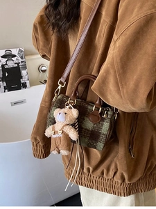 Green and brown plaid cylinder crossbody bag with cute teddy bear charm on a model