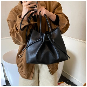 Detail of black textured faux leather bucket bag showing unique knotted strap handle