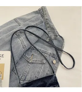 Close-up of a dark denim crossbody bag featuring a slim cylindrical shoulder strap