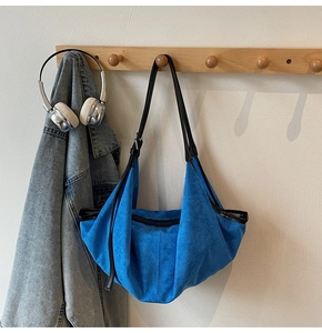 Detail of royal blue suede tote bag with black leather straps hanging on a wooden hook rack
