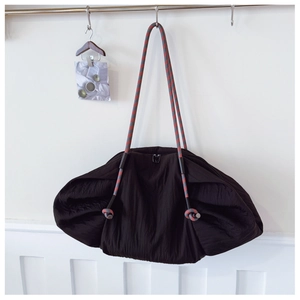 Détail d'un grand sac cabas froncé noir avec des bretelles en corde tressée rouge et gris