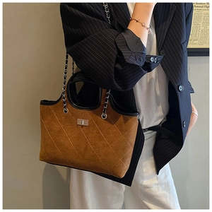 Model wearing a brown quilted suede tote bag with silver clasp and leather chain strap