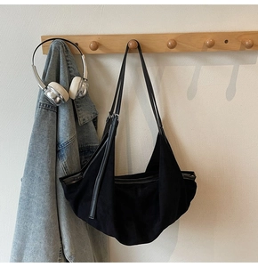 Detail of a large black vintage tote bag hanging on a hanger with denim jacket and headphones