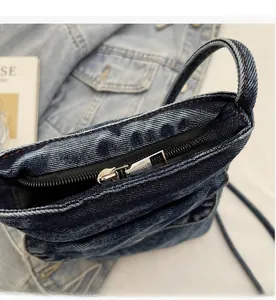 Detail of smooth metal zipper and orange stitching on washed blue denim crossbody bag