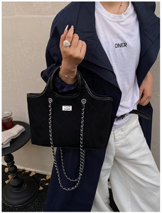 Detail of black quilted tote bag with silver metal swivel lock and suede texture