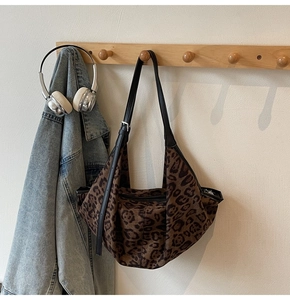 Detail of leopard print hobo bag with adjustable black strap on a wooden hook