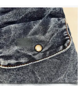 Detailed macro view of dark blue denim fabric with orange stitching and vintage button