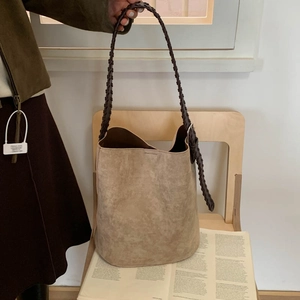 Detailed view of brown suede bucket bag featuring thick woven strap on wooden chair