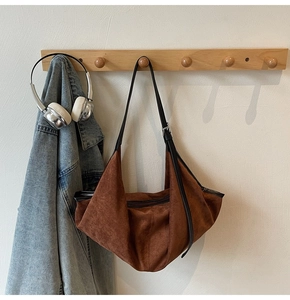 Brown vintage suede tote bag hanging on wooden hook with denim jacket and headphones