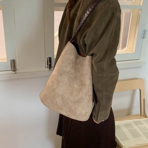 Detail of a large beige suede tote bag featuring a woven strap and hobo bucket style