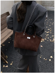 Detail of dark brown suede tote with diamond stitching and metal chain in autumn setting