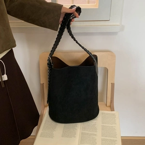 Detail of a large black suede bucket bag with wide woven strap and metal ring connectors