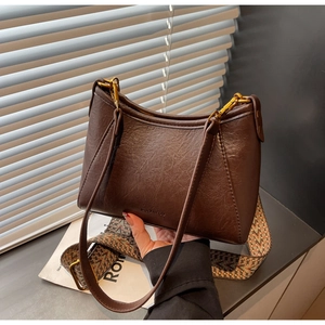 Close-up of deep brown leather shoulder bag with wide geometric woven strap detail