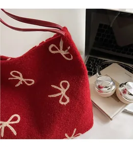 Détail du sac cabas en peluche rouge avec nœuds brodés et anses en cuir dans un décor de bureau