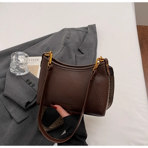 Close-up of vintage brown leather bucket bag with golden hardware and woven shoulder strap