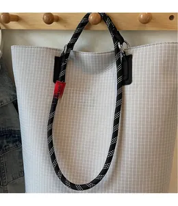 Detail of black and white woven rope strap with silver metal rings on a grey tote bag