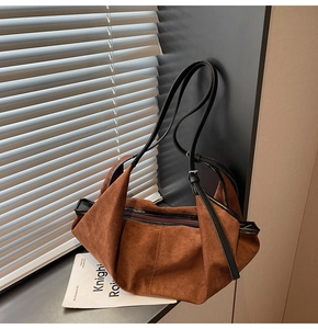 Detailed view of a brown suede hobo bag with adjustable strap on a window sill