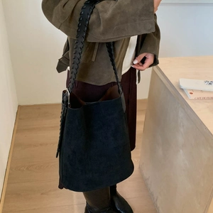 Close-up of a black suede bucket bag with a detailed woven leather shoulder strap on a table