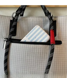 Detail of grey checkered canvas tote bag showing exterior zipper pocket with woven handle