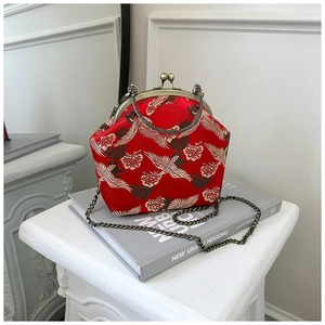 Macro detail of red silk bag featuring crane embroidery and bronze metal clasp closure