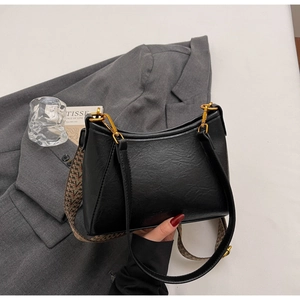 Detail view of black leather shoulder bag featuring gold hardware and chic patterned wide strap