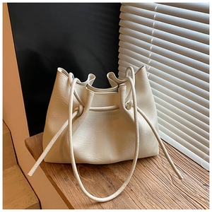 Detail der cremefarbenen Schultertasche mit Kordelzug-Knoten auf Holzstufen