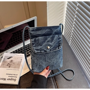 Detail of blue denim phone bag featuring a metal snap button and slim shoulder strap