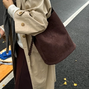Detail of a dark brown suede bucket bag featuring a unique braided shoulder strap texture