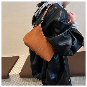 Detailansicht der braunen Wildledertasche mit Goldlogo auf schwarzer Lederjacke
