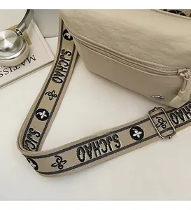 Détail d'un sac bandoulière beige en nylon avec large sangle logo et fermeture éclair