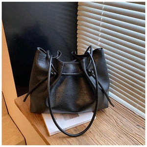 Details einer schwarzen Tote-Bag aus Kunstleder mit Kordelzug auf Holzoberfläche