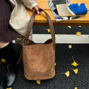 Detail of caramel suede bucket bag with wide stitched strap in autumn setting