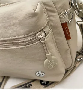 Détail du zip métallique et du badge logo sur le sac bandoulière en nylon beige