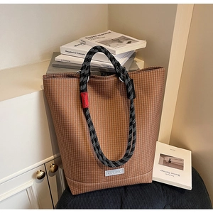 Detailed view of brown checkered canvas tote bag with woven rope handles on a chair