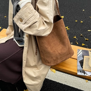 Close-up of brown suede bucket bag featuring a unique braided handle in an autumn setting