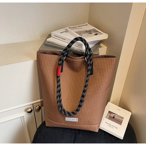 Detail of a brown plaid tote bag with bicolor rope handles and silver brand logo