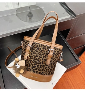 Detail of leopard print bucket bag featuring brown leather trim and a plush monkey charm