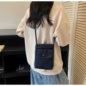 Detail view of small dark blue denim crossbody phone bag with silver snap button closure
