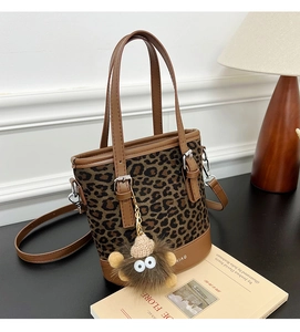 Detailed view of leopard print bucket bag with brown leather trim and plush pendant