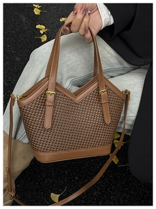 Detail of a brown woven tote bag with V-shaped opening and gold hardware on pavement