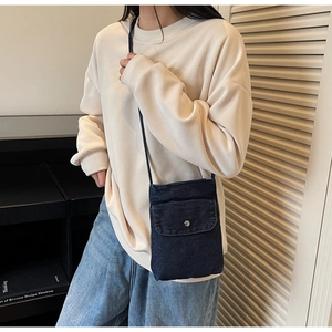 Detail of blue denim mini crossbody bag with silver button on a white sweatshirt