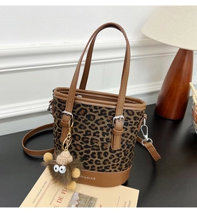Detail view of leopard print bucket bag with leather trim and plush charm on desk