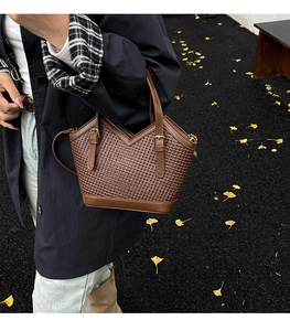 Close-up of brown woven tote bag with gold metal buckles on an autumn street background